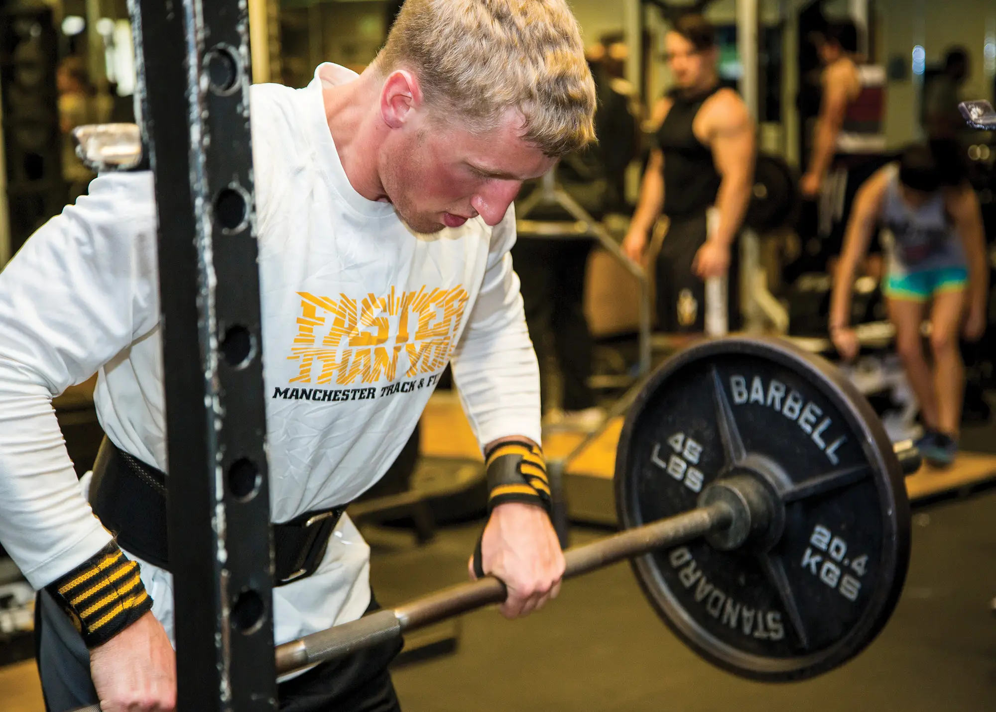 Student in gray shirt and yellow writing lifting large weight