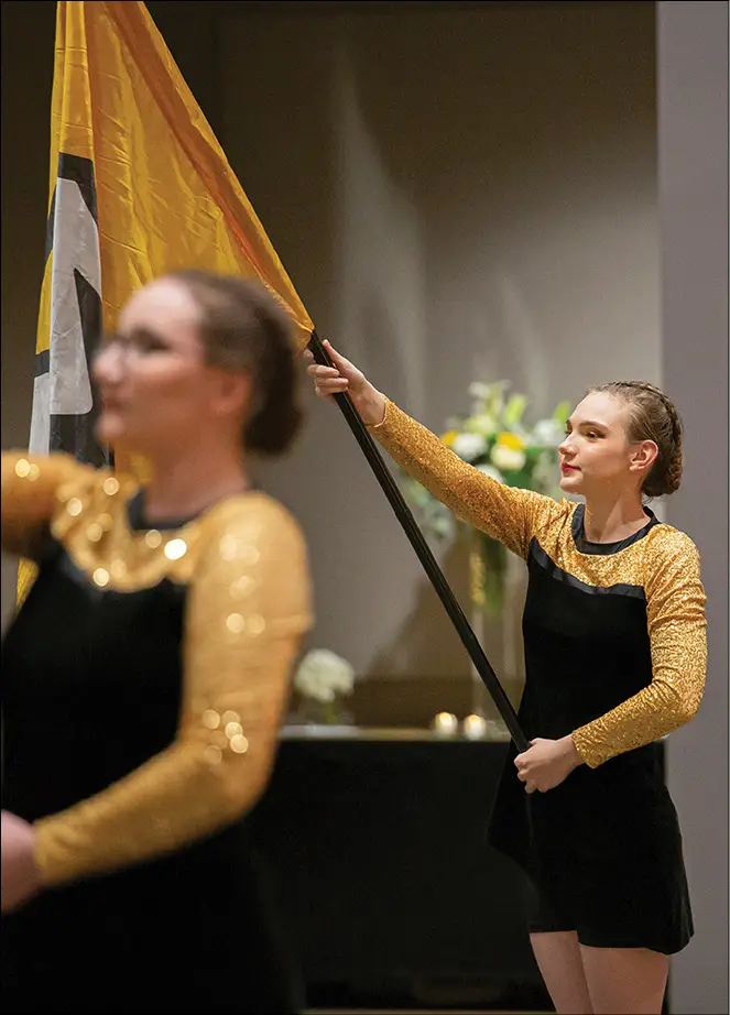 Two color guard members with one in and one out of focus holding gold flags