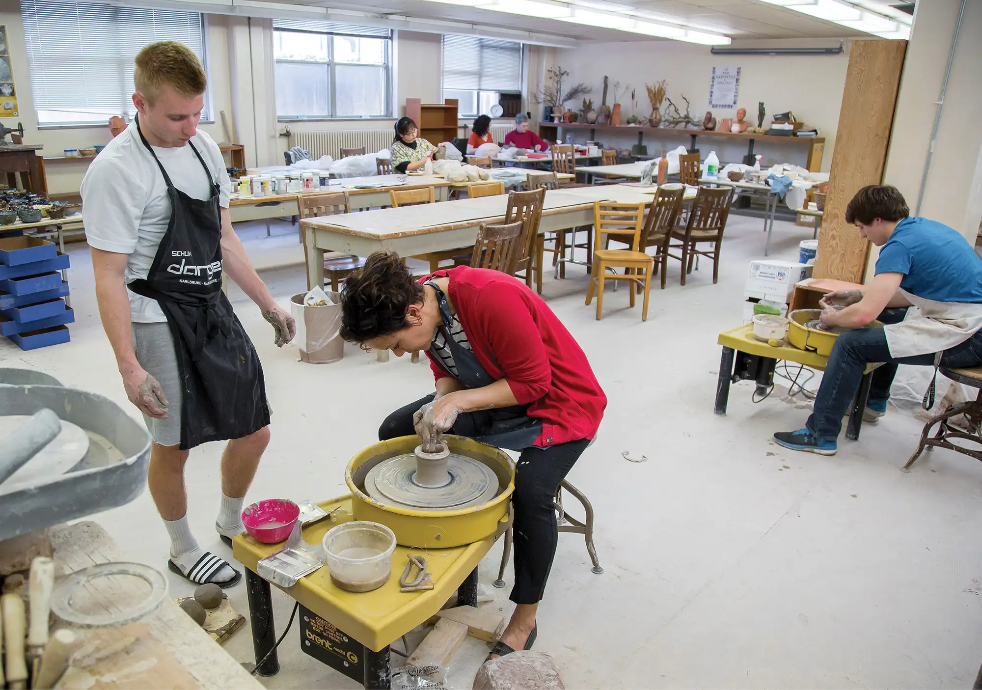 Art class where student is watching teacher on pottery wheel