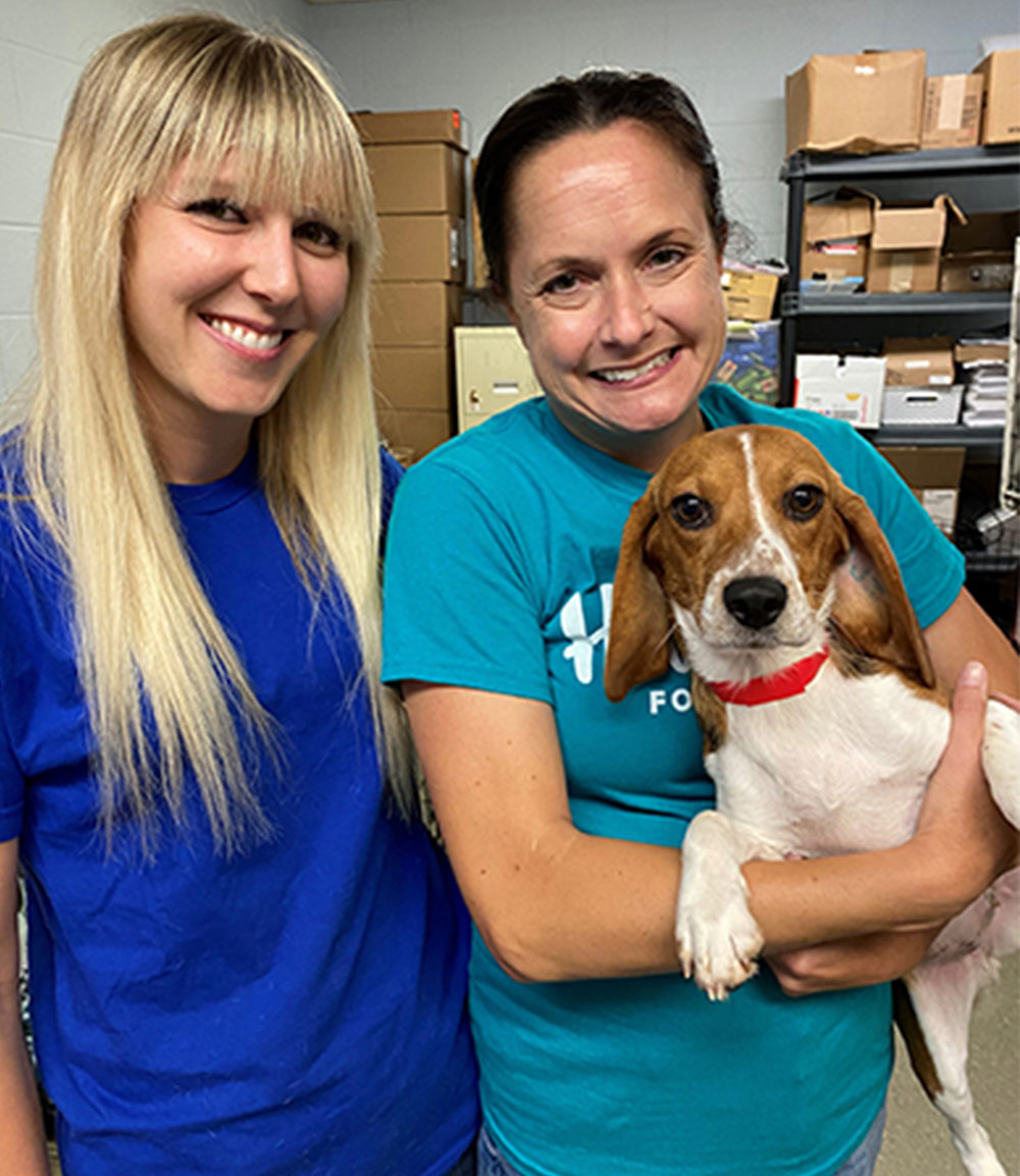 Samantha Chapman and Stacy Erickson-Pesetski stand together for a photo while Stacy Erickson-Pesetski holds a beagle in her arms