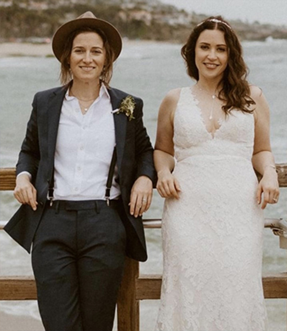 Tiffany Berkbile Numbers and Andrea Numbers stand together for a wedding photo on a pier