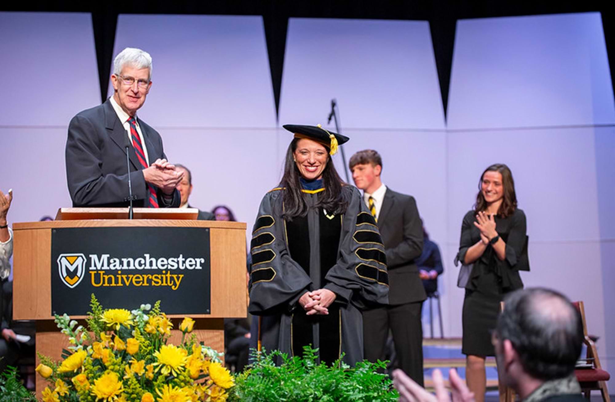 Dr. Stacy Hendricks ’96 Young dressed in full doctoral regalia stands smiling on stage during her inauguration as university president